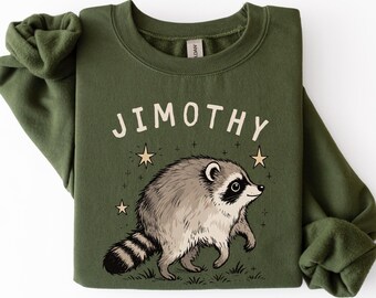Könnte beinhalten: Ein olivgrünes Sweatshirt mit Rundhalsausschnitt und einer grafischen Illustration eines Waschbären auf Gras. Über dem Waschbären ist der Text JIMOTHY in einer cremefarbenen serifenlosen Schrift gedruckt, umgeben von kleinen Sternen.