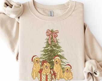 Könnte beinhalten: Ein beigefarbenes Sweatshirt mit Rundhalsausschnitt und einem Grafikdruck eines grünen Weihnachtsbaums, der mit einer rot-weiß gestreiften Schleife verziert ist. Vier Golden Retriever mit roten Weihnachtsmützen sitzen am Fuß des Baumes.