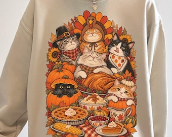 Könnte beinhalten: Ein beigefarbenes Sweatshirt mit Rundhalsausschnitt und einem farbenfrohen Grafikdruck, der mehrere für Thanksgiving gekleidete Katzen zeigt, umgeben von Kürbissen, Sonnenblumen, Herbstblättern, einem gebratenen Truthahn, Maiskolben und verschiedenen Kuchen.