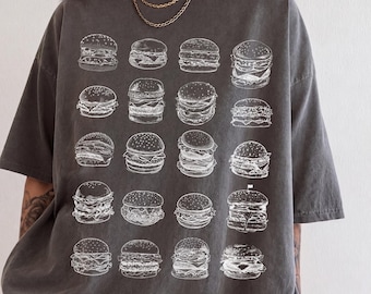 Könnte beinhalten: Ein anthrazitfarbenes Kurzarm-T-Shirt mit einem weißen Grafikdruck von zwanzig verschiedenen Burger-Illustrationen in einem Rastermuster. Das Shirt hat einen Rundhalsausschnitt und eine lockere Passform mit verschiedenen Burger-Stilen.