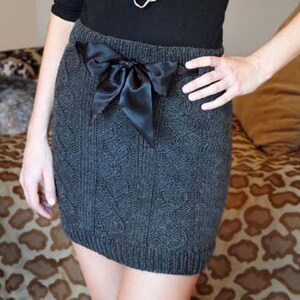 May include: A charcoal grey, cable-knit mini skirt featuring a black satin bow at the waist. The skirt has a textured, patterned design. The bow provides a stylish contrast to the knitted fabric, creating a chic look.