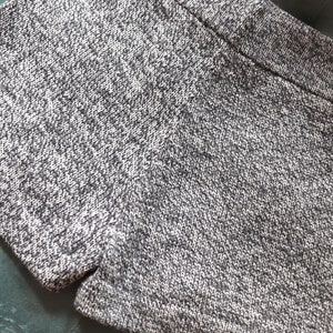 May include: Close-up of gray knit shorts. The shorts have a textured appearance with a mix of light and dark gray threads. The garment is folded, showcasing the waistband and the fabric's detailed weave. The shorts appear to be made of a soft, comfortable material.