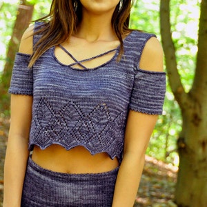 May include: A blue and white striped knit crop top with a criss-cross neckline and cold shoulder design. The top is made of a soft, lightweight fabric and has a scalloped hem.
