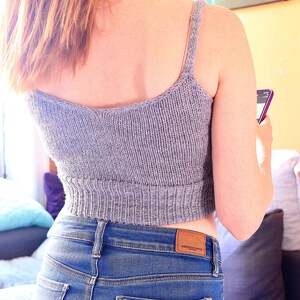 May include: A gray knitted crop top with thin straps. The top is worn with blue jeans and the label "American Eagle" is visible on the back of the jeans.