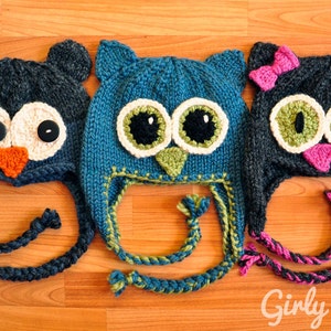 May include: Three knitted owl hats with different colored yarn and embellishments. The hats are blue, teal, and gray with white, green, and pink accents. The hats have long ties that can be tied under the chin.