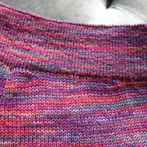 Peut inclure: Gros plan sur un tissu tricot&eacute; avec un motif ray&eacute; multicolore dans des tons de rose, violet et bleu.