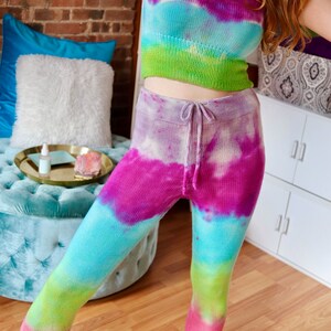 Peut inclure: Un haut court en tricot tie-dye et un legging assorti dans des tons de rose, violet, bleu et vert. Le haut a un col rond et des bretelles fines. Le legging a une taille &eacute;lastique avec cordon de serrage.