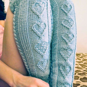 May include: A pair of light blue knitted leg warmers with a heart pattern.