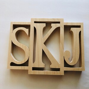 May include: Wooden wall decor with the letters "SKJ" cut out in a simple, modern font.