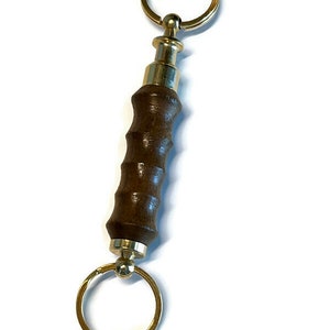 May include: A brown wooden keychain with a brass ring and a brass swivel. The keychain is about 4 inches long.