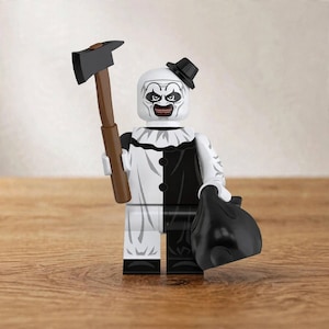 May include: A plastic minifigure of a clown character with a white face, black eye makeup, and a wide grin. The figure wears a black and white split-color outfit with a ruffled collar, a small black top hat, and holds a brown-handled axe and a black bag.