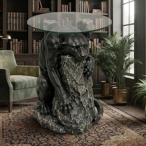 Könnte beinhalten: Ein runder Beistelltisch mit Glasplatte und einem skulpturalen Sockel in Form eines schwarzen Panthers, der auf einem strukturierten grauen Felsen kauert. Der Panther stützt mit seinen Vorderpfoten auf dem Stein das runde Glasplattenteil.