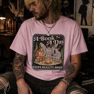 Een boek per dag houdt de realiteit op afstand (T-shirt), T-shirt voor boekenliefhebbers, T-shirt met leesprint, T-shirt met cryptidenboek, T-shirt met Mothman, Bigfoot en herten