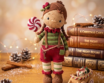 May include: A crocheted doll with brown hair, wearing a green and red striped shirt, red shorts with suspenders, and a small key attached to the waist. The doll holds a red and white swirled lollipop. A small crocheted sled with a gift sits nearby.