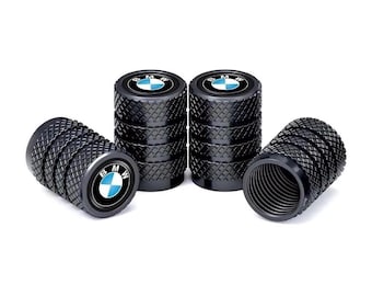 Puede incluir: Cuatro tapones de válvula de neumático cilíndricos de color negro con una textura de patrón de diamante. Cada tapón presenta un logotipo circular de BMW en la parte superior con colores azul, blanco y negro. Tienen un interior roscado.