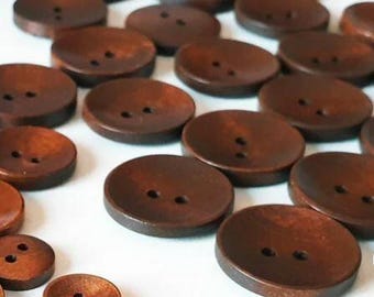 May include: A collection of brown wooden buttons with two holes each. The buttons are arranged in a random pattern on a white surface.