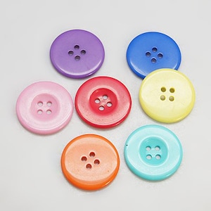 May include: Assortment of colorful plastic buttons with four holes each. The buttons are in shades of purple, pink, red, yellow, blue, and orange.