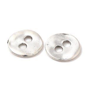 May include: Two silver-coloured, round buttons with three holes each. The buttons have a slightly textured surface and a vintage appearance. These buttons are suitable for sewing projects and crafts.