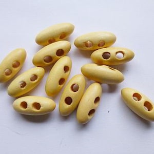 May include: A group of ten yellow wooden buttons with two holes each. The buttons are oval shaped and have a smooth finish.