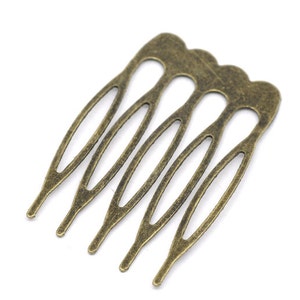 May include: A gold-toned metal hair comb with five teeth. The teeth are shaped like elongated ovals with a decorative cutout design.