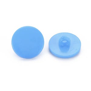 Puede incluir: Dos botones redondos de color azul claro. Uno muestra una superficie lisa y plana. El otro revela un ojal para coser. Estos botones son adecuados para proyectos de costura.