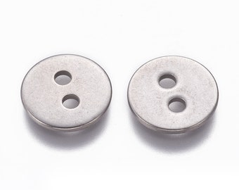 Op de afbeelding: Twee zilveren metalen knopen met elk twee gaten. De knopen zijn rond en hebben een glad oppervlak.