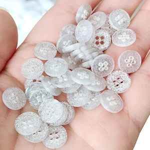 May include: A pile of small, clear, sparkly buttons with four holes each. The buttons are translucent and have a subtle shimmer.