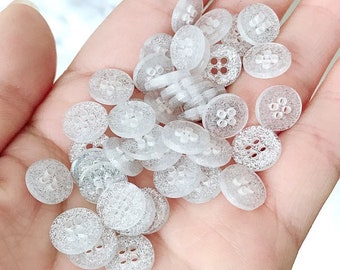 May include: A pile of small, clear, sparkly buttons with four holes each. The buttons are translucent and have a subtle shimmer.