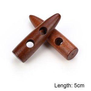 May include: Two brown wooden toggle buttons with two holes each. The buttons are 5 cm long.