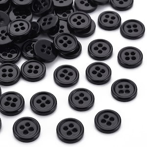 May include: A large group of black plastic buttons with four holes each. The buttons are scattered on a white surface.