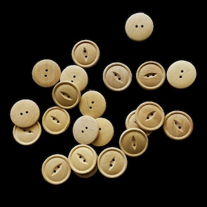 May include: A collection of light brown wooden buttons with two or three holes. Some buttons have two holes, while others have a single, elongated hole. The buttons are round and vary slightly in color and grain pattern.