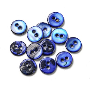 May include: A collection of twelve round, two-hole buttons featuring a vibrant blue, iridescent finish. Several buttons display dark, textured patches of natural shell material, while others show a smooth, glossy, and reflective surface.