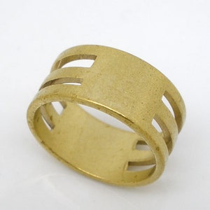 May include: A gold-toned ring with a wide band and three horizontal cutouts. The ring has a smooth, matte finish.