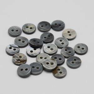 May include: A collection of 20 gray shell buttons with two holes each. The buttons are round and have a slightly iridescent finish.