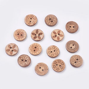 Könnte beinhalten: Sortiment von 14 Holz-Knöpfen mit verschiedenen gravierten Designs, darunter Sterne, Blumen und geometrische Muster. Die Knöpfe sind hellbraun und haben jeweils zwei Löcher.