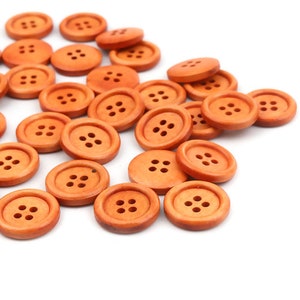 Op de afbeelding: Een verzameling oranje houten knopen met verschillende aantallen gaten. De knopen zijn willekeurig gerangschikt op een witte achtergrond.