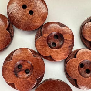 Könnte beinhalten: Nahaufnahme mehrerer Holzknöpfe mit blütenförmigem Design. Die Knöpfe sind in einem satten, rötlich-braunen Farbton gehalten und haben zwei Löcher zum Annähen. Die Knöpfe sind rund und haben eine leicht strukturierte Oberfläche.