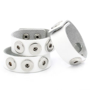 May include: Three white leather snap button bracelets with silver snaps. The bracelets are stacked on top of each other.
