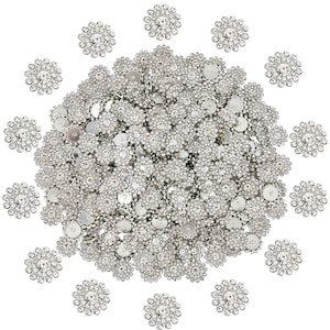 May include: A collection of silver-toned, rhinestone-studded embellishments. The embellishments are circular, with a central rhinestone surrounded by smaller stones, resembling flowers. The image shows a large pile of these decorative pieces, with some scattered around.