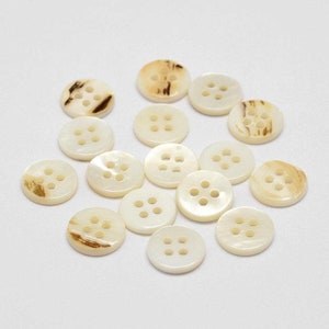 May include: A collection of 15 white and brown shell buttons with four holes each.