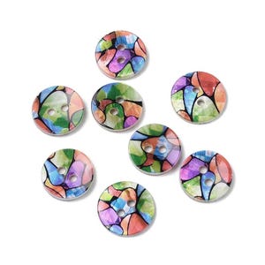 May include: A collection of eight round buttons with a colorful stained-glass design. The buttons feature a variety of colors, including red, orange, green, blue, and purple. Each button has two holes for sewing and is approximately 0.75 inches in diameter.