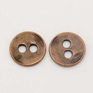 May include: Two copper-colored buttons with two holes each. The buttons have a slightly textured surface.