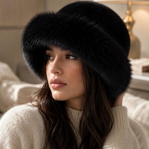 May include: A solid black bucket hat crafted from a dense, plush faux fur material. The hat features a rounded crown and a wide, downward-sloping brim that provides full coverage. The texture of the material is uniform, soft, and deep black.