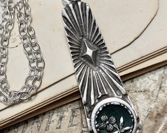 May include: A silver necklace with a pendant featuring a starburst design and a black cameo with a floral motif.