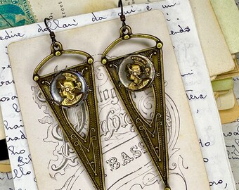 May include: A pair of brass triangle-shaped earrings with a cameo-style image of a woman's face in the center of each triangle. The earrings have a vintage look and are perfect for adding a touch of elegance to any outfit.