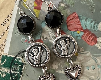 May include: A pair of dangle earrings with black faceted beads, silver cherub charms, and silver heart charms.
