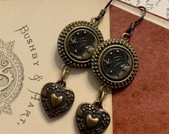 May include: A pair of bronze earrings with a crescent moon and star design. Each earring has a small heart charm hanging from it.