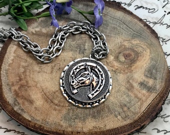 May include: Silver necklace with a round pendant featuring a horse head design. The pendant has a textured surface and a horseshoe shape around the horse's head.