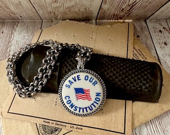 May include: A silver chain necklace with a round pendant featuring an American flag and the words "Save Our Constitution".