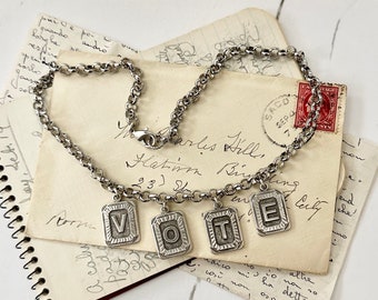 May include: A silver necklace with four charms spelling out the word "VOTE". The necklace is on top of a stack of old, handwritten letters.